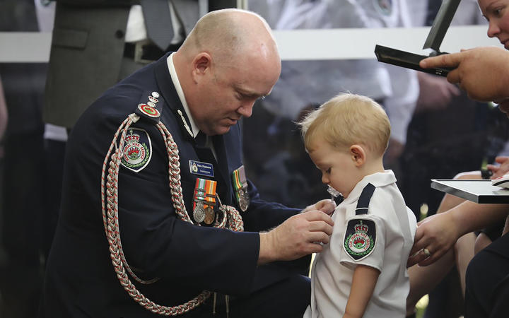 Australian Rural Fire Service Commissioner Shane Fitzsimmons pinning a medal on Geoffrey Keaton's son Harvey. 