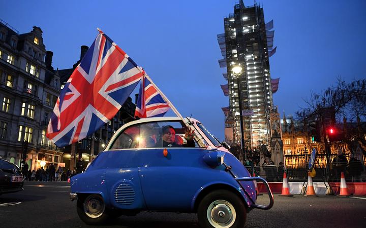 A man waves Union flags from a small car as he drives past Brexit supporters gathering in Parliament Square, near the Houses of Parliament in central London on Brexit day.