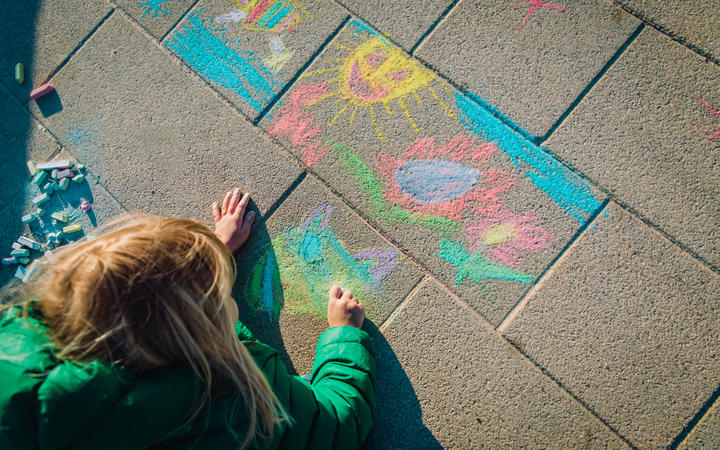 Child drawing outside on footpath with chalk.