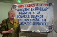 Robyn in front of the banner from the Ivory Coast which reads (roughly translated) 'Beat disability. Honour New Zealand for your fight for disabled people.'