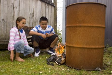 Two youngsters stare at a small fire lit from a bundle of paper