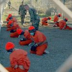 Detainees in orange jumpsuits sit in a holding area of Guantanamo Bay prison camp